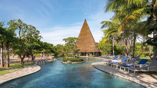 A pool area with lounge chairs, a thatched-roof structure, and tropical vegetation.