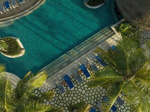 Vista aérea de un resort con piscina cristalina, sillones de descanso y palmeras.