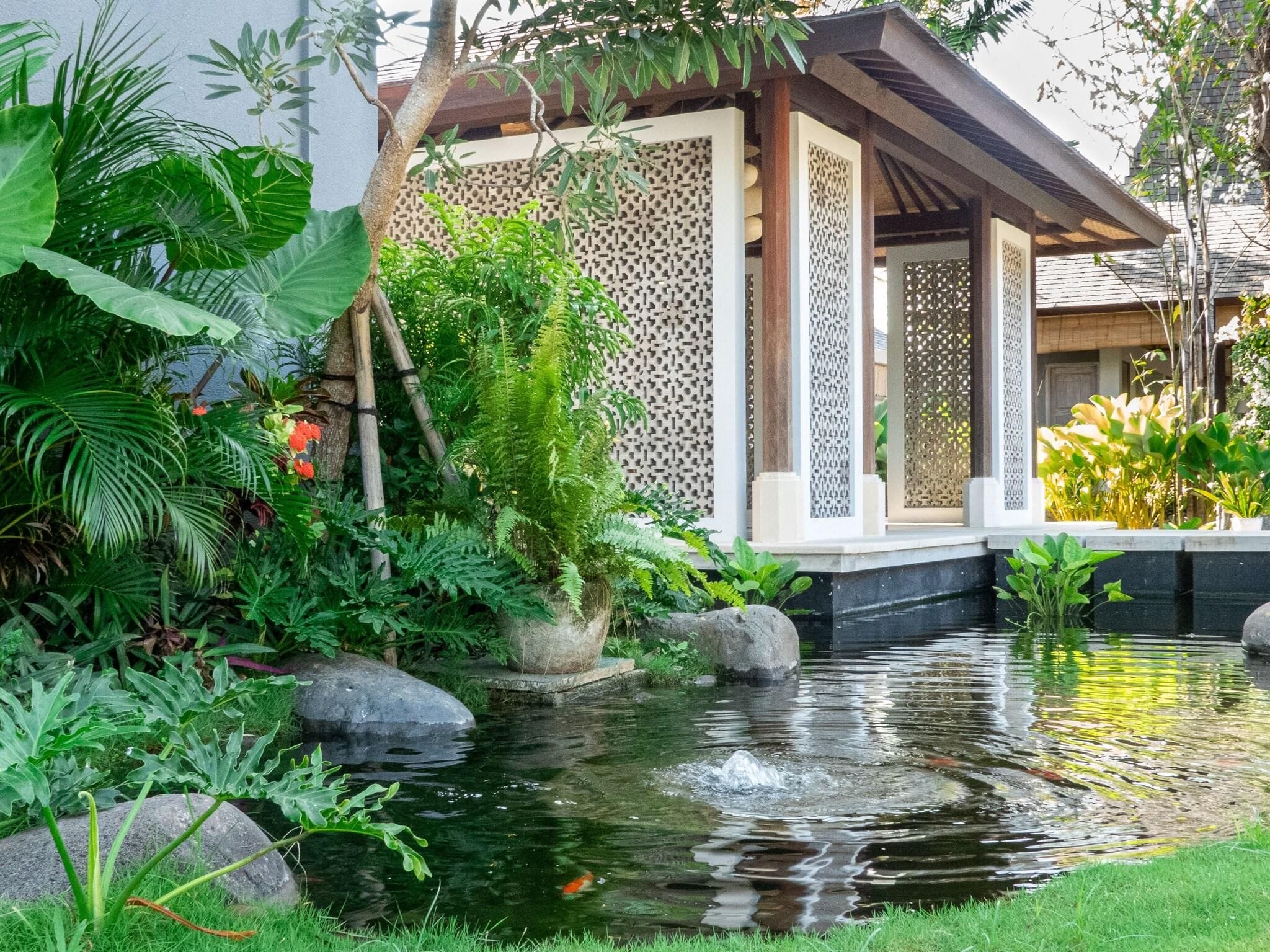 A tranquil garden with a pond, lush greenery, and a traditional wooden structure.