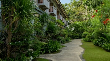 A pathway leading to a building with balconies, surrounded by lush greenery and tropical plants.