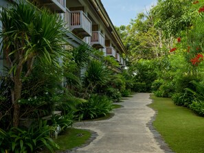 Un camino que lleva a un edificio con balcones, rodeado de exuberante follaje y plantas tropicales.