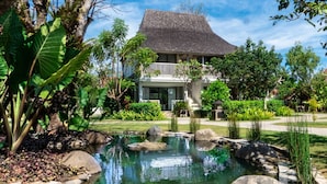 A large house with a balcony, surrounded by a garden with a pond and rocks.