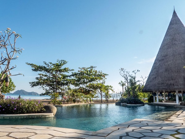 A resort pool area with a clear view of the sea, a thatched-roof structure, and a landscaped garden.