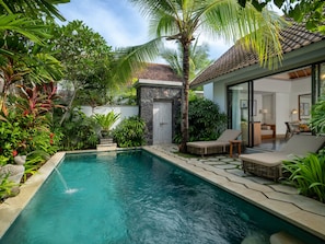 A swimming pool with lounge chairs, surrounded by tropical plants and a stone wall.