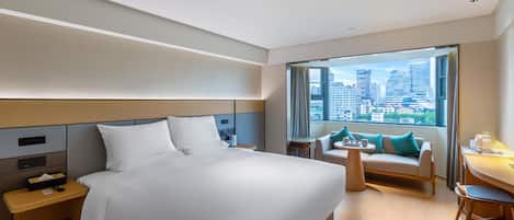 A hotel room with a large bed, a sofa, a small table, and a view of the city.