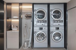 Un espace buanderie compact comprenant quatre machines à laver superposées, un sèche-linge et un sèche-mains.