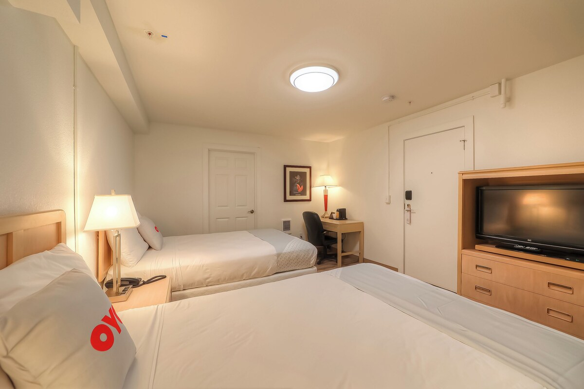 A hotel room with two beds, a desk with a lamp, a television, and a door.