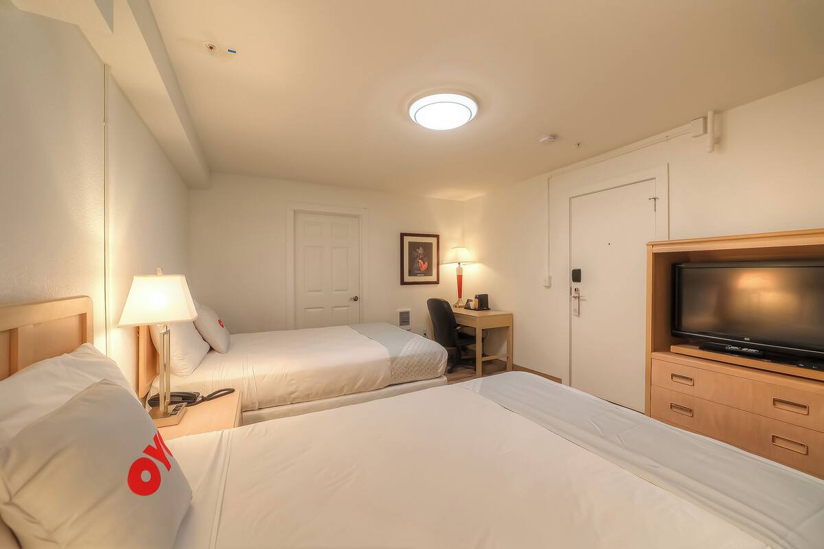 A hotel room with two beds, a desk with a lamp, a television, and a door.