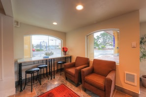 A kitchen with a bar area, two bar stools, a brown leather chair, and a window with a view of a parking lot. - Newport Inn By OYO - Hwy 101 (Mapleton)