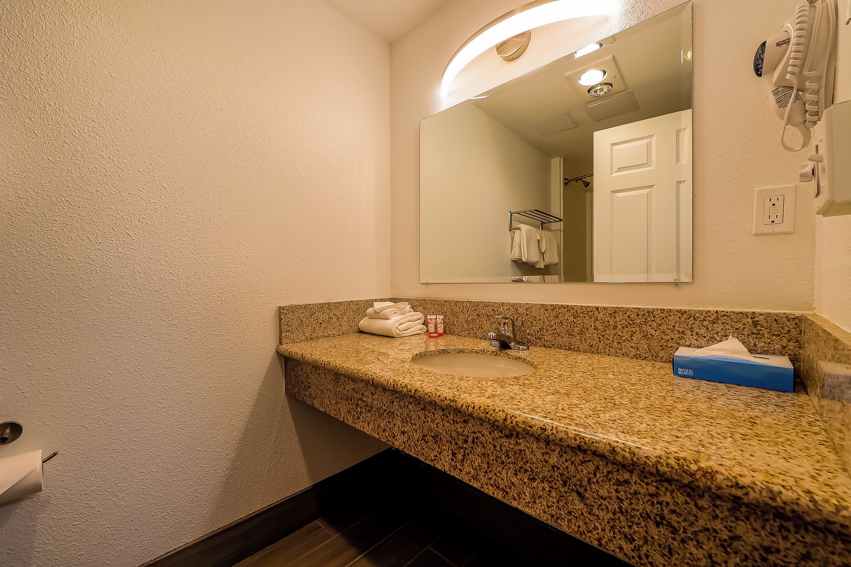 A bathroom with a granite countertop, a sink, a mirror, a towel rack, and a hairdryer.