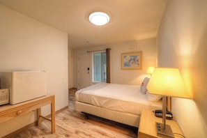 A hotel room with a bed, bedside lamp, telephone, and a small table with a refrigerator.