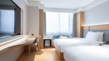 Habitación de hotel con cama, escritorio, silla y ventana con cortinas.