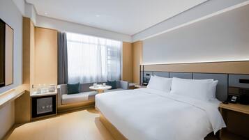 A modern hotel room with a large bed, a small seating area, a bedside table, and a window with curtains.