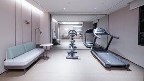 A modern gym with exercise equipment, a seating area, and a hallway leading to another room. - Ji Hotel (Chengdu)