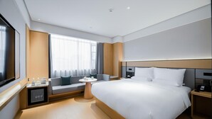 A modern hotel room with a large bed, a bedside table, a small table with a chair, a sofa, and a large window with curtains. - Ji Hotel (Chengdu)