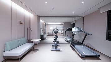 Een moderne fitnessruimte met trainingsapparatuur, een zithoek en een gang naar een andere ruimte.