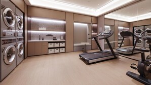 A modern hotel room with a built-in washer and dryer, a treadmill, and a small seating area. - Ji Hotel (Yantai)