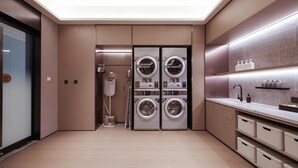 A modern laundry room with two stacked washing machines, a drying machine, and a sink with storage baskets. - Ji Hotel (Yantai)