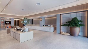 A modern hotel lobby with a reception desk, a large potted plant, and a wall-mounted digital display. - Ji Hotel (Yantai)