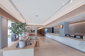 Eine moderne Hotelhalle mit Empfangstresen, einer Pflanze und einem digitalen Informationsbildschirm.