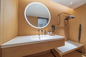 Ein modernes Badezimmer mit einem großen Spiegel, einem Waschtisch, einem Handtuchhalter, einem Fön und einer Dusche.