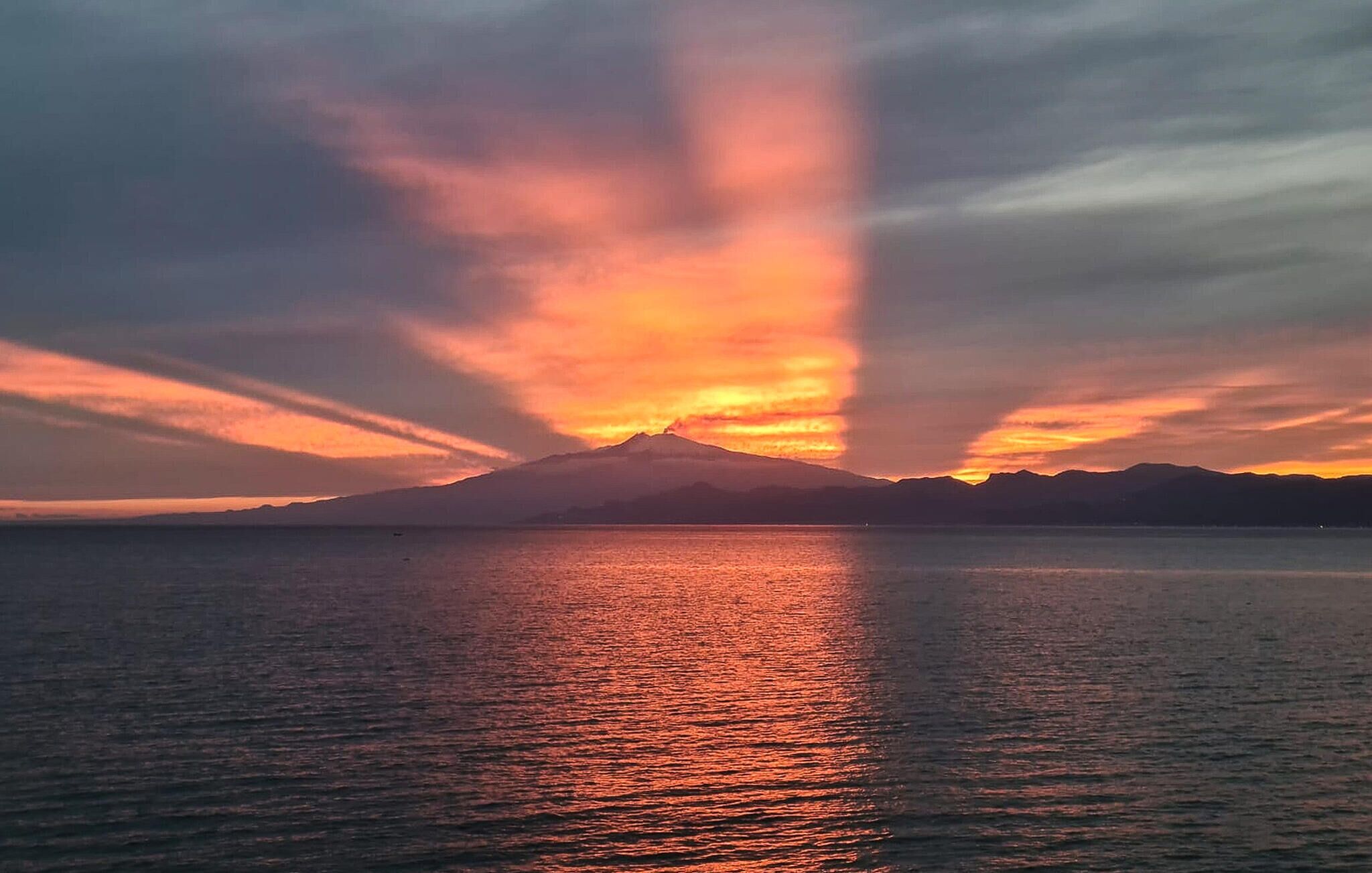 A sunset over a body of water with a mountain in the background.