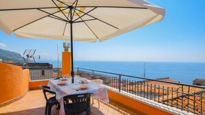 Une terrasse avec une table dressée pour le repas, un grand parasol et une vue sur la mer.