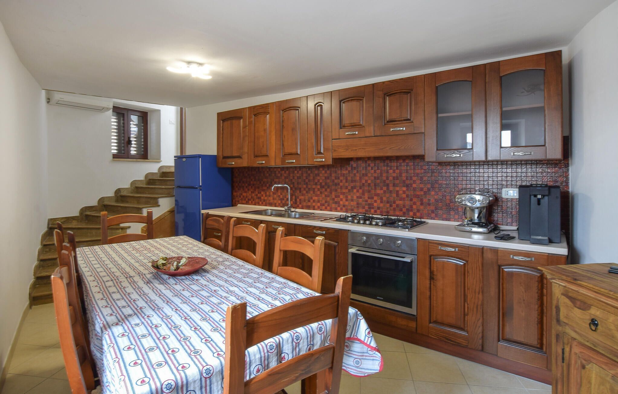 A compact kitchen with wooden cabinets, a blue refrigerator, a gas stove, and a dining table with chairs.