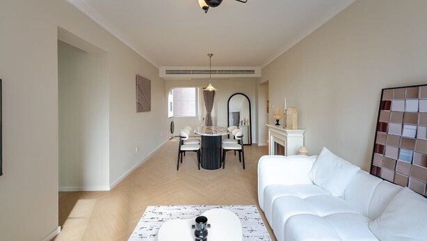 Ein modernes Wohnzimmer mit einem weißen Sofa, einem runden Esstisch mit Stühlen, einer Kristallleuchtre und einem Kamin.