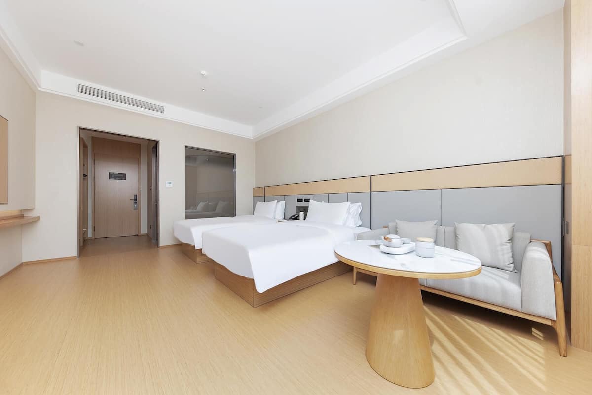 Ein Hotelzimmer mit zwei Betten, einem Sofa, einem runden Tisch und einer Tür zu einem weiteren Raum.
