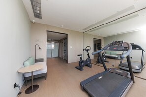 Ein Hotelzimmer mit Bett, kleinem Schreibtisch, Laufband, Hometrainer und Waschmaschine.