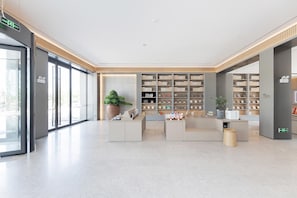 A modern lobby with a reception desk, a large potted plant, and a bookshelf filled with books. - Ji Hotel (shaoxing Shangyu Economic Development Zo (Shaoxing)