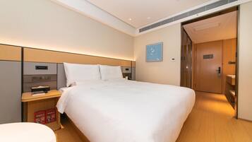 A hotel room with a large bed, a bedside table with a lamp, a small desk, and a trash bin.