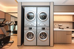 Un moderno lavadero con cuatro lavadoras y secadoras apiladas, una encimera con un lavabo y una cinta de correr al fondo.