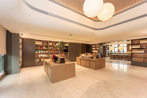 A modern hotel lobby with a central reception desk, shelves with books and decorative items, and a seating area with tables and chairs. - Ji Hotel (Xi'an)