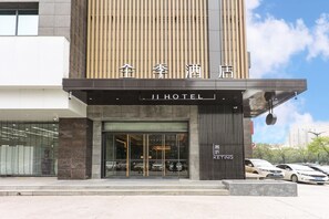Een hotelentree met een modern ontwerp, met een grote glazen gevel, een opvallend bord en een parkeerplaats met verschillende auto's.