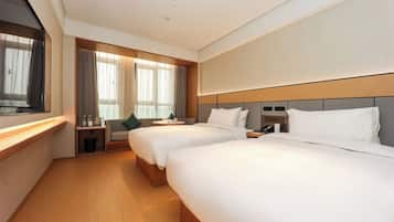 A hotel room with two beds, a bedside table, a nightstand, a window with curtains, and a television.