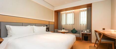 A hotel room with a large bed, a desk, a chair, a small table, and a window with curtains.