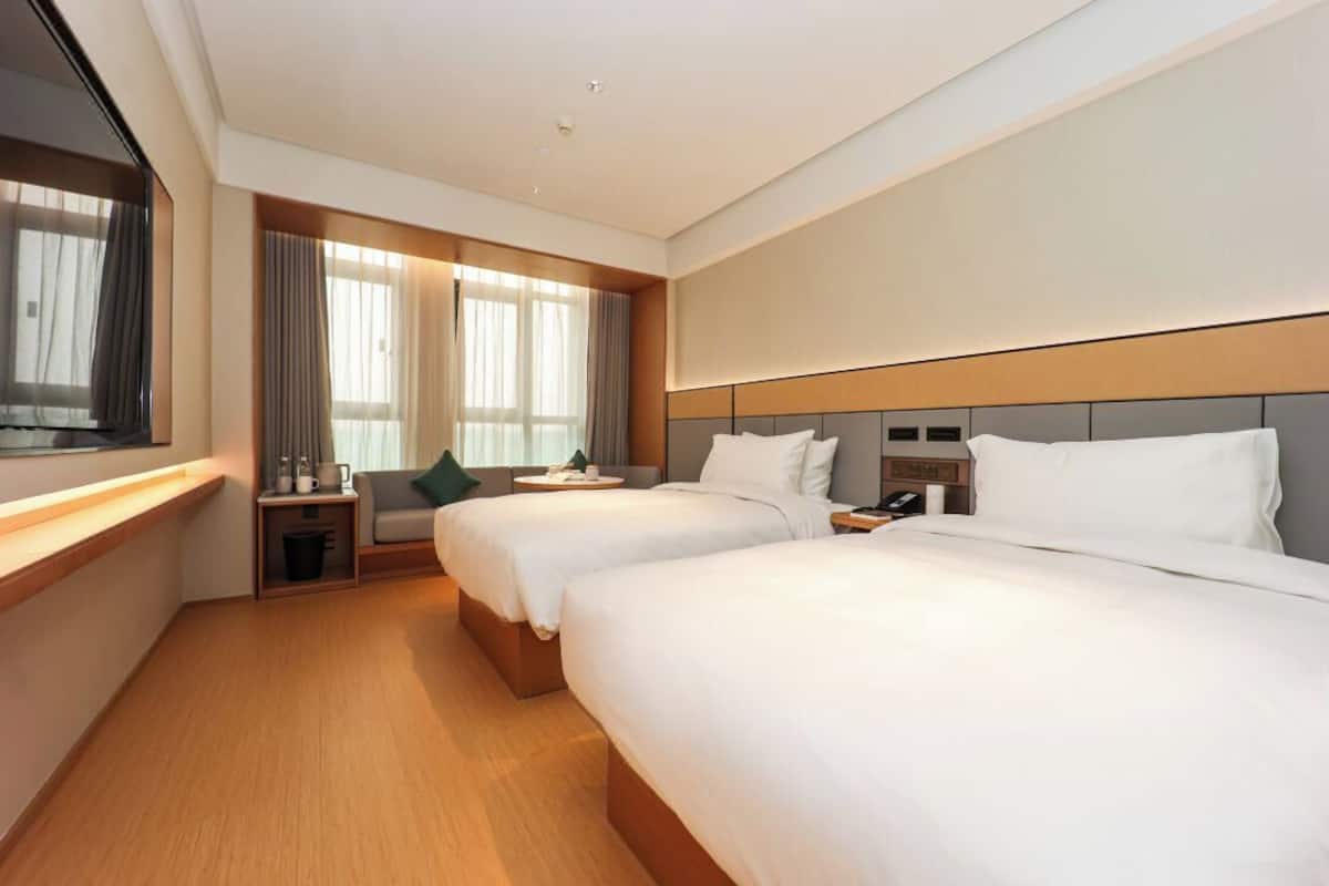 Habitación de hotel con dos camas, una mesita de noche, un ventanal con cortinas y un televisor.
