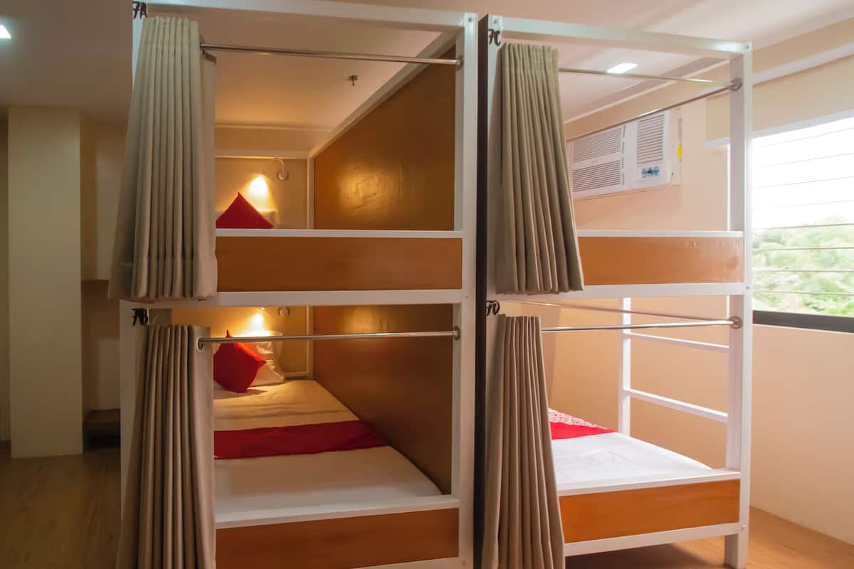 Dormitorio con literas, cortinas, suelo de madera y ventana con persianas.