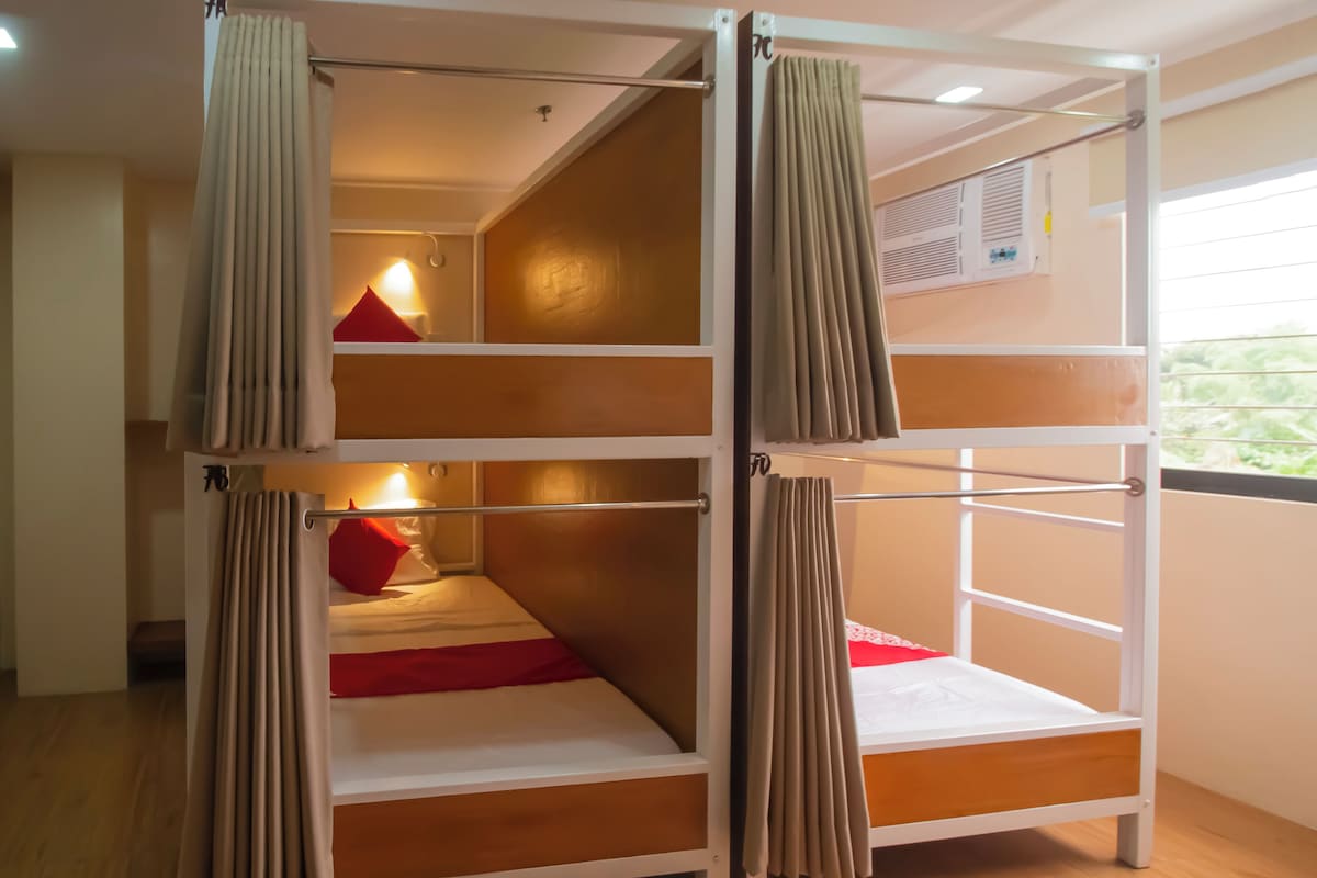 A bunk bed room with curtains, a wooden floor, and a window with blinds.