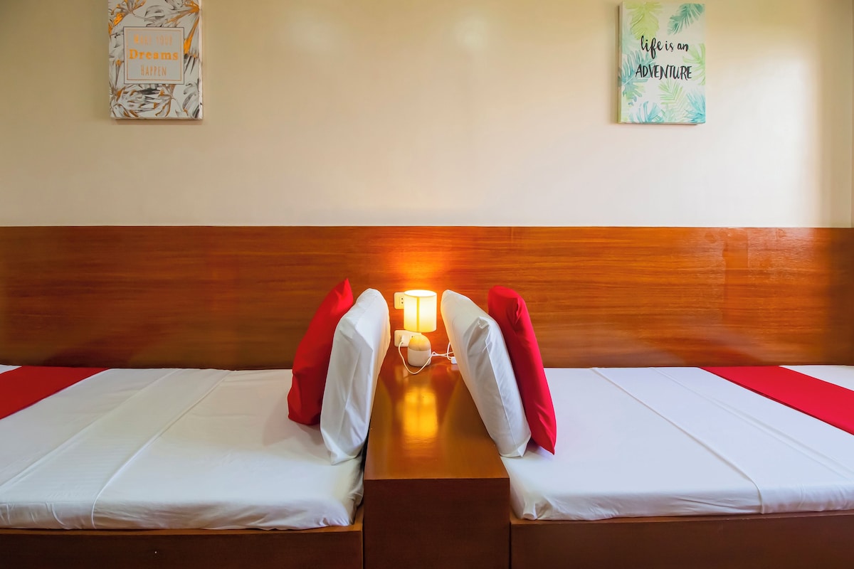 A hotel room with two single beds, a wooden headboard, a bedside table with a lamp, and motivational posters on the walls.