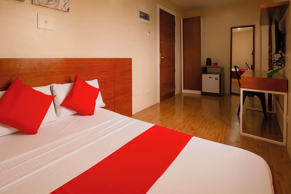 Habitación de hotel con una cama grande, cabecera de madera, un escritorio pequeño y un espejo.