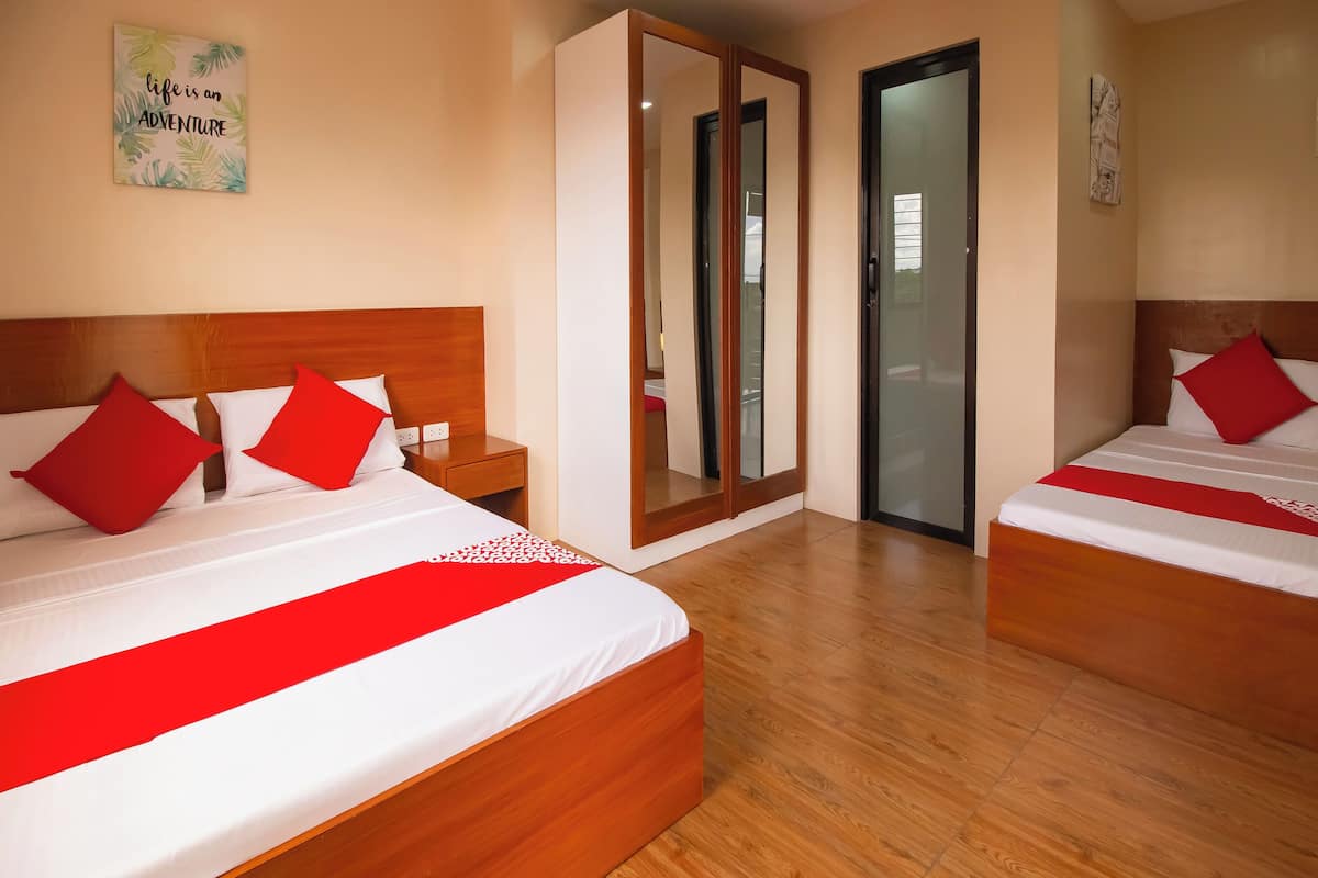Habitación de hotel con dos camas, cada una con cabecera de madera, ropa de cama blanca y almohadas rojas. Hay un espejo en una pared y una puerta que da a otra habitación.