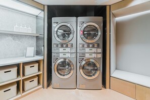Une buanderie équipée de quatre machines à laver superposées, d’une étagère contenant des articles de toilette et d’une armoire en bois.