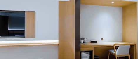A modern hotel room with a bed, a desk, a chair, a small refrigerator, and a window.