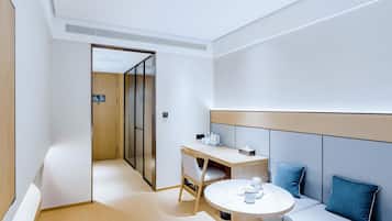 Ein modernes Hotelzimmer mit einem Holztisch, einem runden Tisch, einer Couch mit blauen Kissen und einer Schiebetür zu einem weiteren Raum.