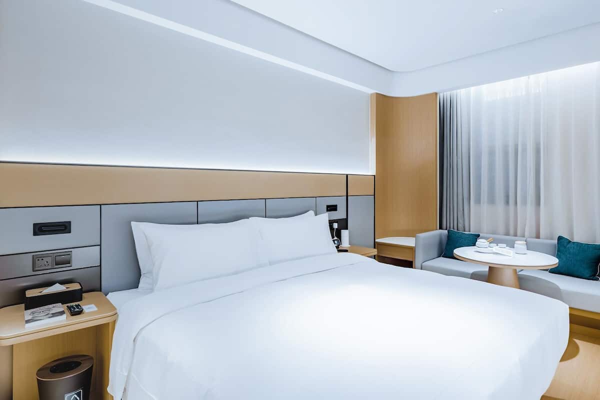 Ett modernt hotellrum med en stor säng, en soffa, ett litet bord och ett fönster med gardiner.