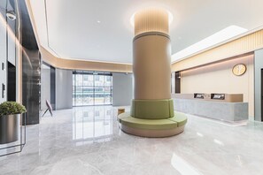 A modern lobby with a central pillar, a reception desk, and a large glass door leading outside. - Ji Hotel (Shanghai)