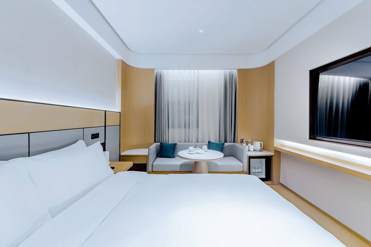 Ett modernt hotellrum med en stor säng, en soffa, ett litet bord och ett fönster med gardiner.
